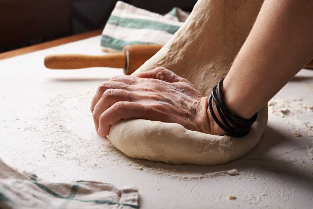 Manos estirando masa con rodillo para preparar tortas fritas uruguayas