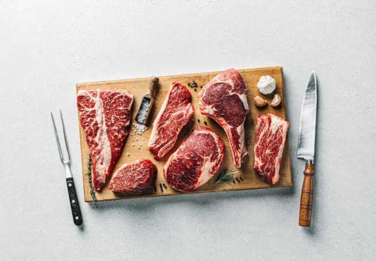 Las mejores carnes de España: chuletones, razas, cortes y maduración 1 Surtido de chuletones y cortes de vacuno crudos sobre una tabla de madera, con vetas de grasa visibles