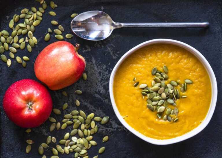 Crema de calabaza asada con manzana y puerro: cremosa y sin nata 1 Cuenco de crema de calabaza asada con manzana y puerro, decorado con pipas de calabaza tostadas y hierbas frescas